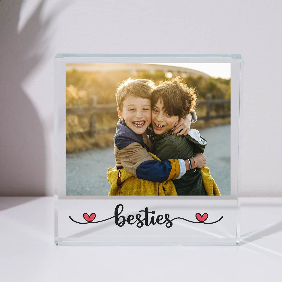 Acrylic photo frame with a photo of two children hugging and the word 'besties' below on a white surface.